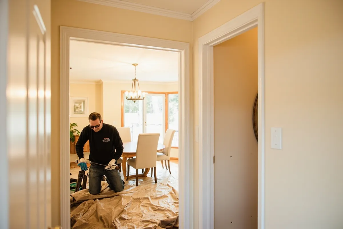 Interior painter taping trim and laying canvas drop cloths in a dining room